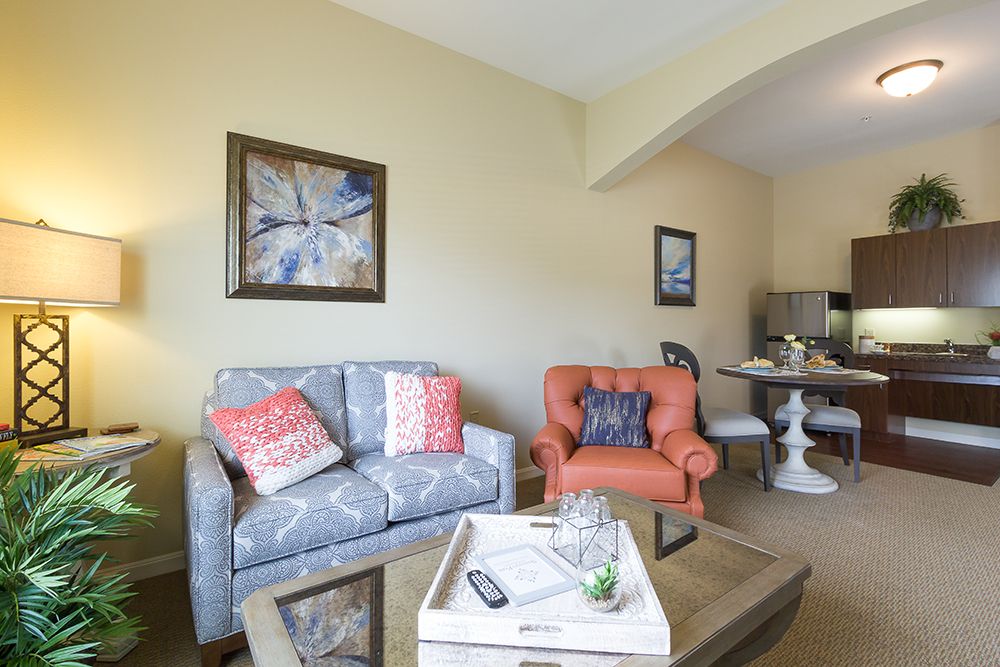 A cozy living room featuring a patterned sofa with colorful cushions, an orange armchair, and a glass coffee table adorned with a decorative tray.