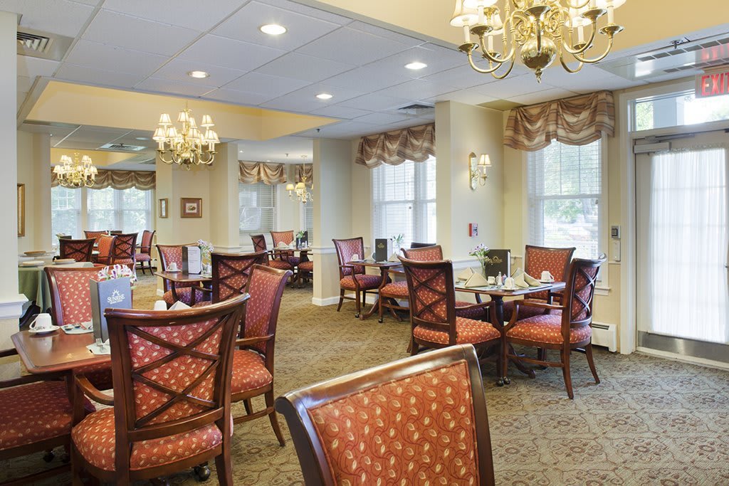 An elegantly decorated dining area with chandeliers, carpeted flooring, and neatly arranged tables and chairs.