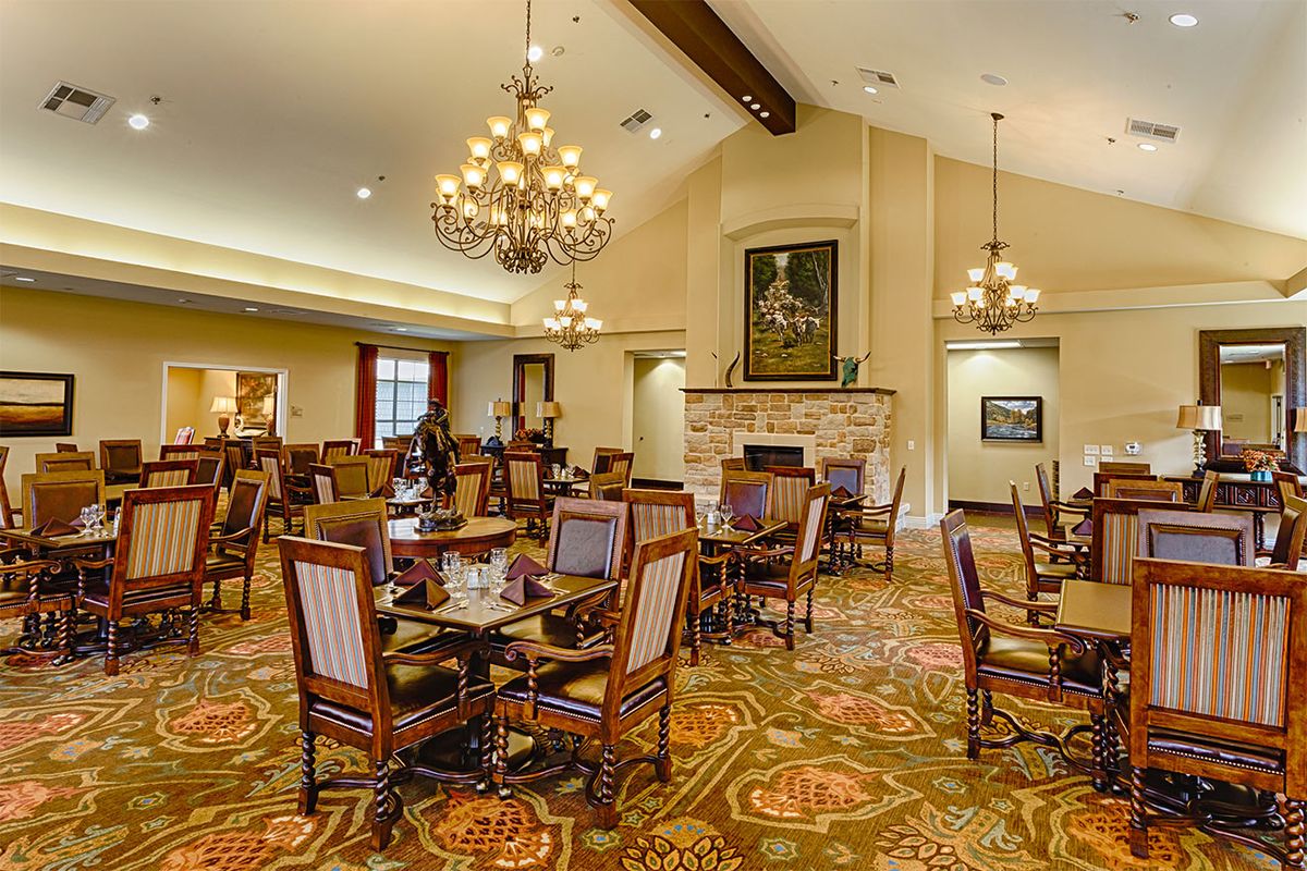 A spacious and elegantly decorated dining room featuring chandeliers, wooden tables and chairs, and a patterned carpet.