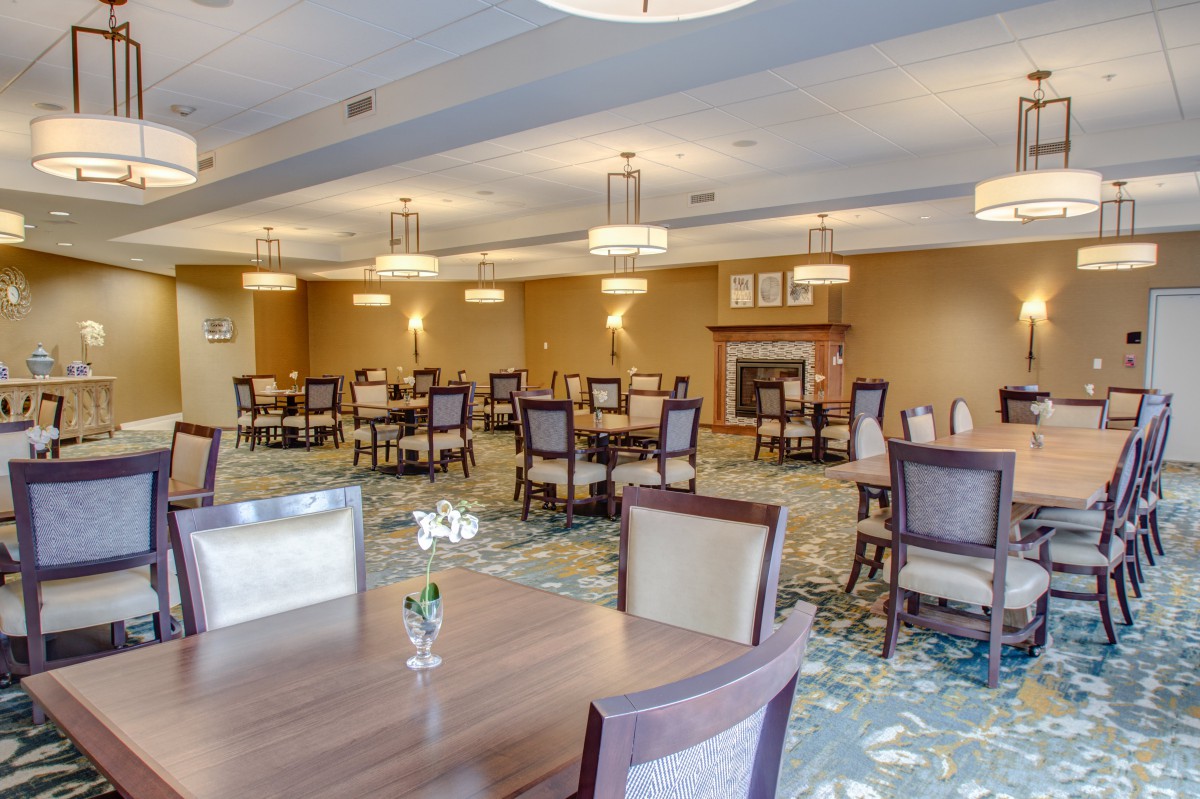 An elegantly furnished dining room with multiple tables and chairs, softly lit by overhead lights.