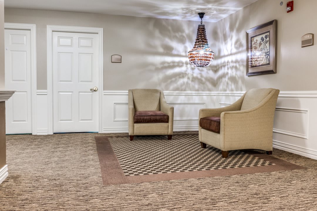 A cozy waiting room with two armchairs, a decorative carpet, and a chandelier.