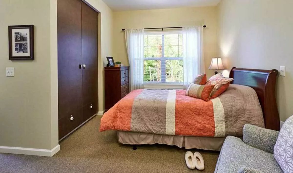 A cozy bedroom with a neatly made bed and colorful bedding, featuring a large window and a wooden closet.