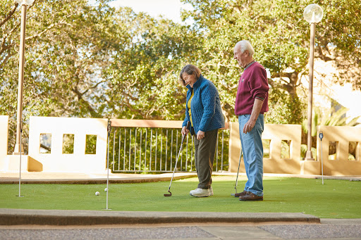 An elderly couple enjoys a game of golf on a sunny day at the putting green.
