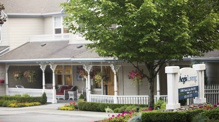 A charming suburban house with a cozy porch adorned with hanging plants and surrounded by trees and flowers.