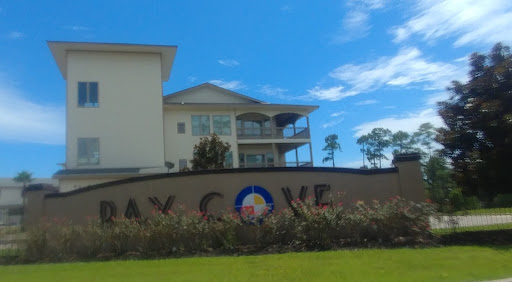 A residential building at Bay Cove, featuring a decorative sign and lush landscaping under a clear blue sky.