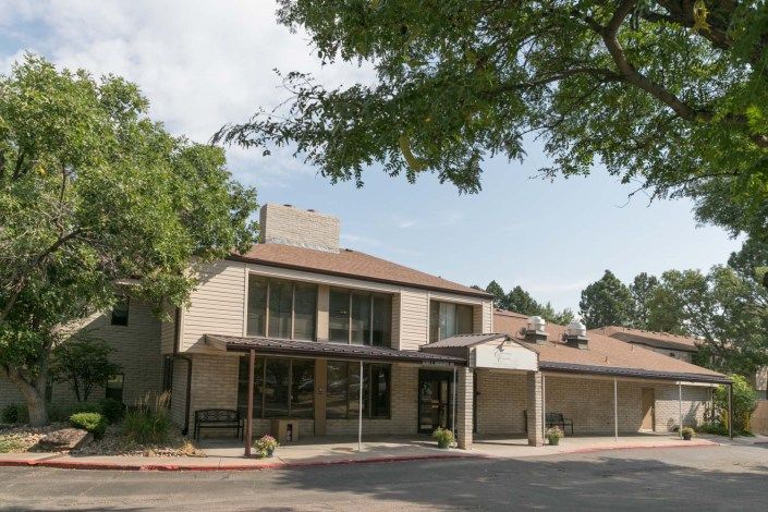 A two-story residential building with a tree in the foreground and a clear sky above.