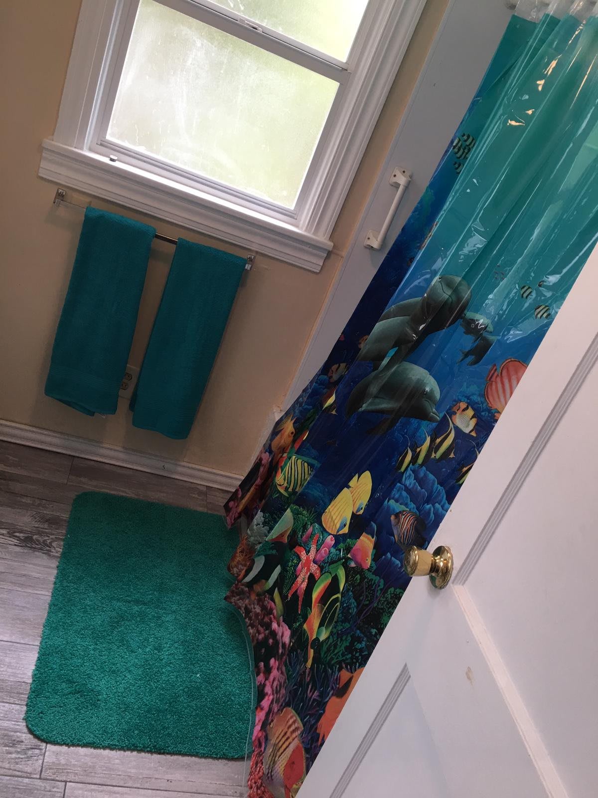 A bathroom featuring an ocean-themed shower curtain, teal towels, and a matching bath mat.