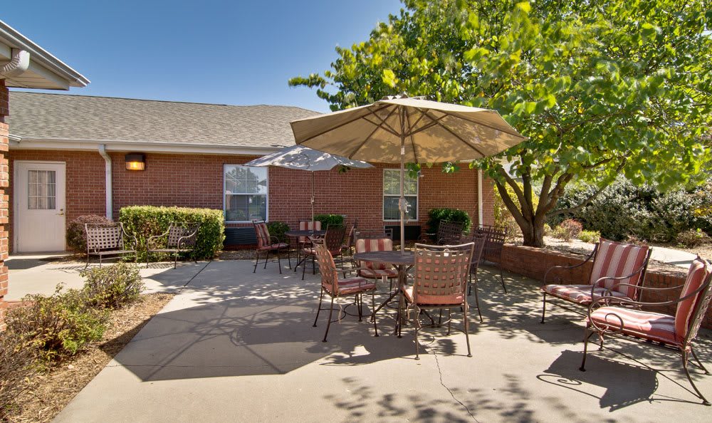 A cozy outdoor patio with tables and chairs under a large umbrella, adjacent to a brick building.