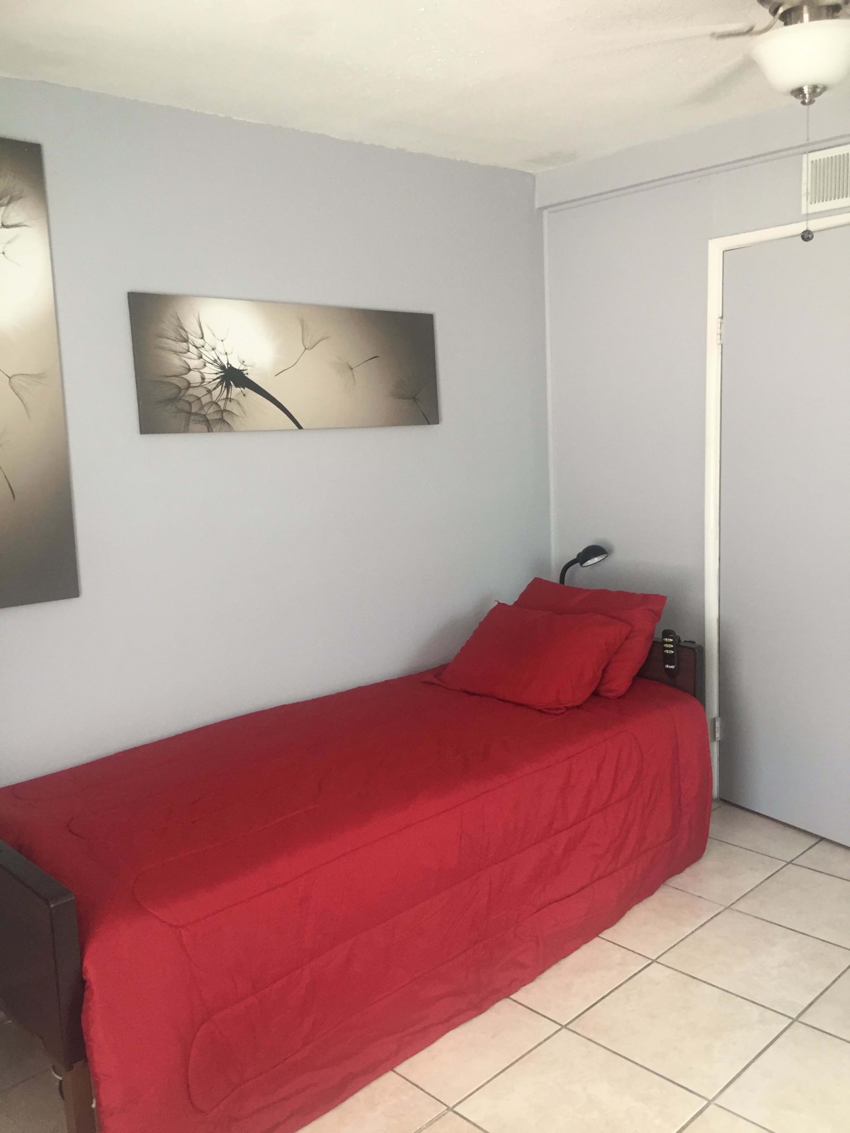 A minimalist bedroom with a single bed covered in red bedding and modern art on the walls.