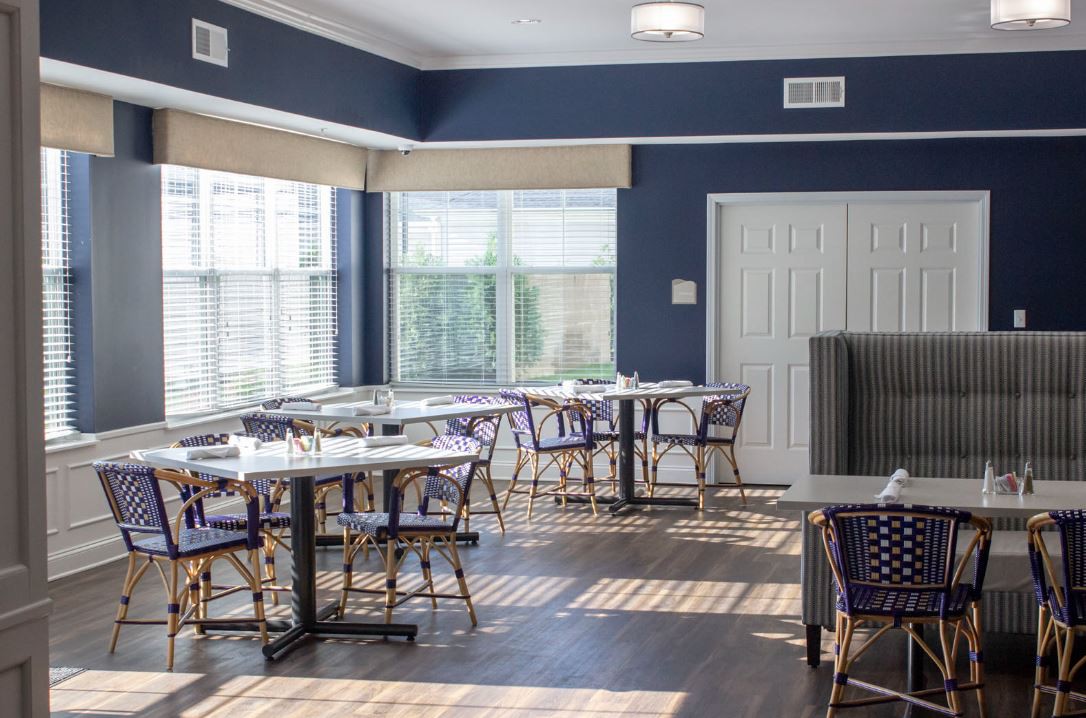 A bright and airy dining area with multiple tables and chairs, illuminated by large windows.