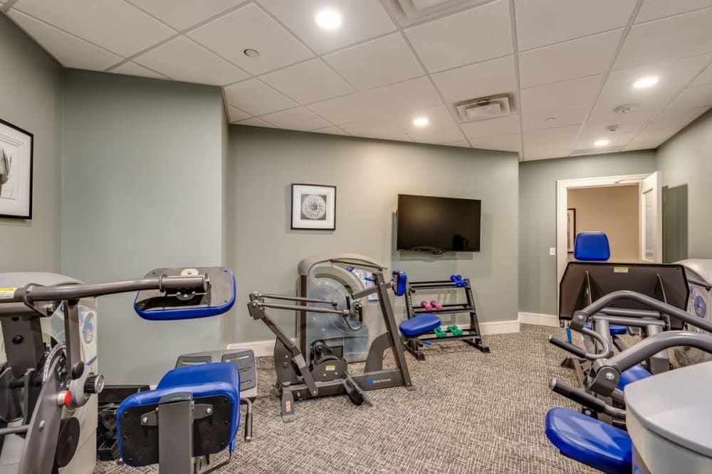 A small gym with various exercise equipment and a television on the wall.
