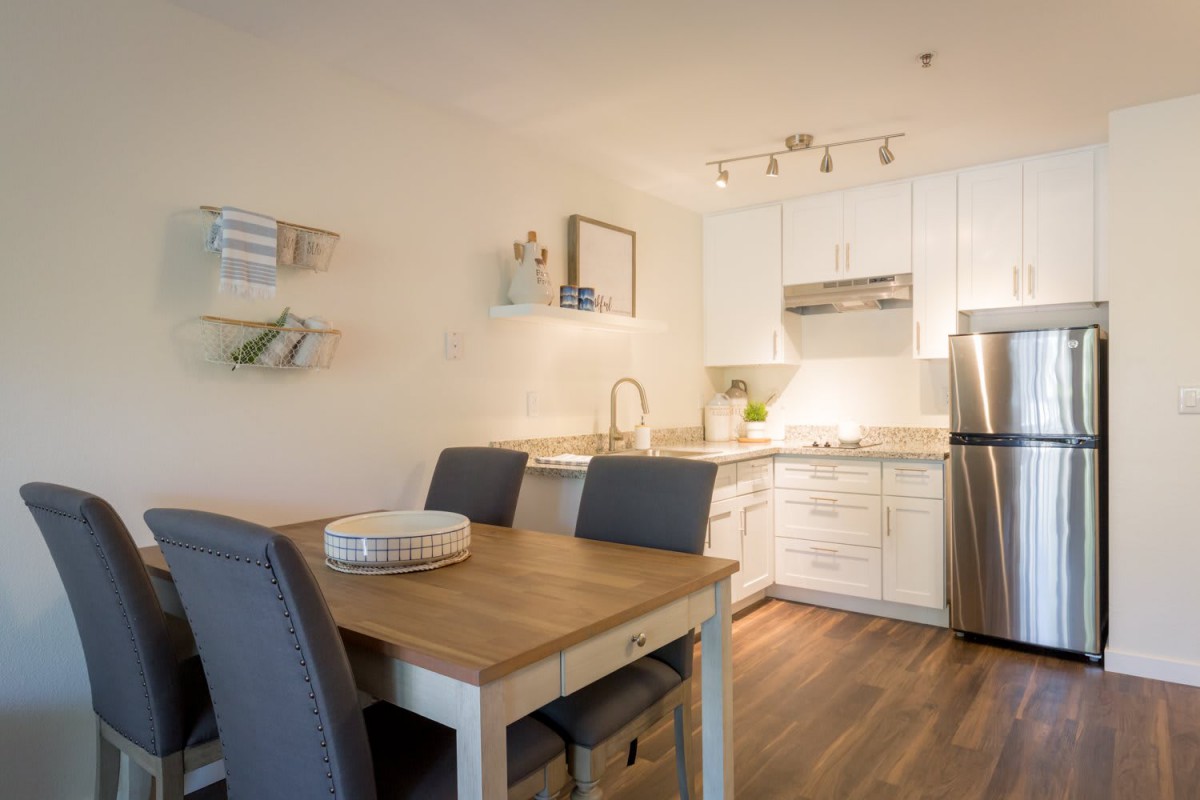 A modern kitchen and dining area with a wooden table, grey chairs, white cabinets, and stainless steel appliances.