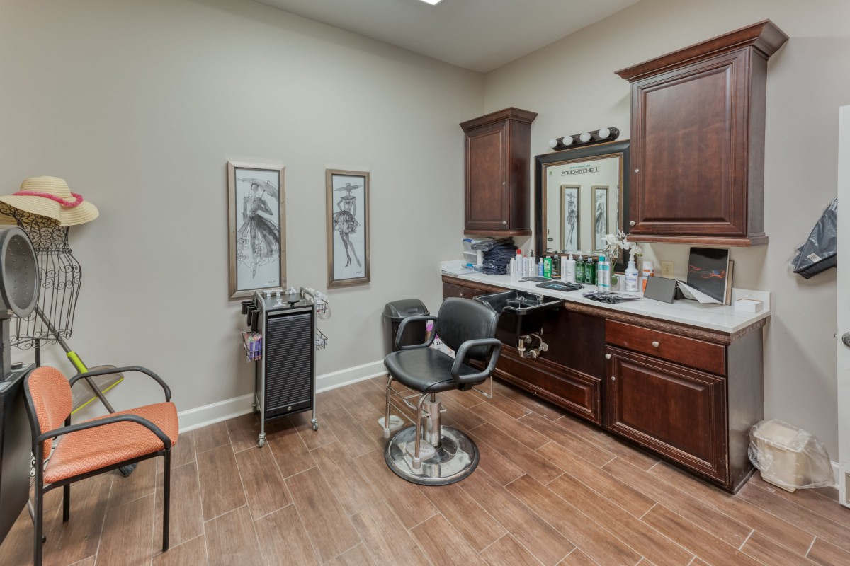 A well-organized hair salon room with a styling chair, mirror, and wooden cabinets.