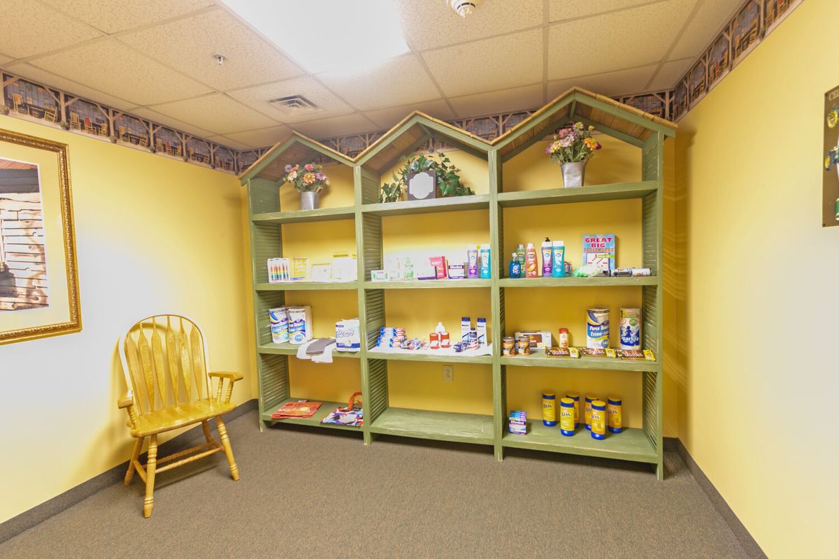 A store display with green shelves showcasing various products against yellow walls, alongside a wooden rocking chair.