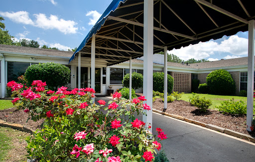 A beautiful view of a building shaded by an awning, surrounded by vibrant pink flowers and lush greenery.