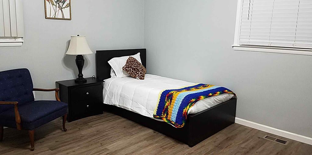 A minimalist bedroom with a single bed, colorful blanket, and a nightstand with a lamp.