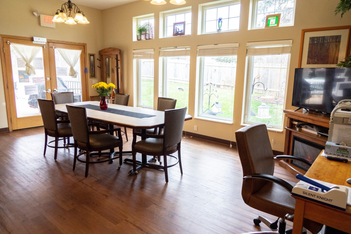A well-lit dining room with a large table and chairs, surrounded by tall windows.