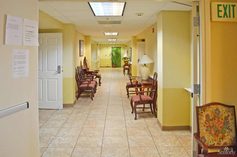 A bright hallway with yellow walls and a tiled floor, featuring chairs arranged in a waiting area.