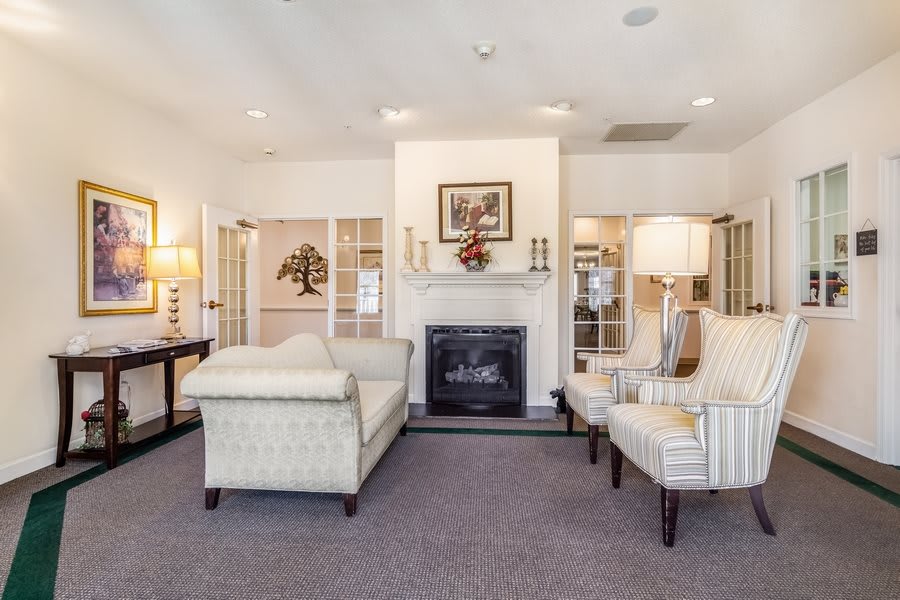 A cozy living room with a fireplace, sofa, and armchairs, featuring traditional decor and artwork.