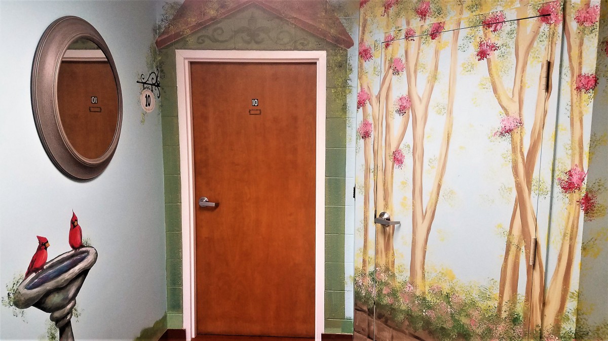 A creatively painted wall featuring a wooden door framed by a mural depicting trees and foliage.