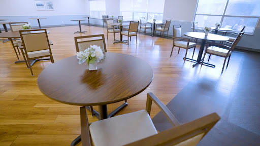 A bright and minimalist dining area featuring wooden tables and chairs, with a small vase of flowers on the table.