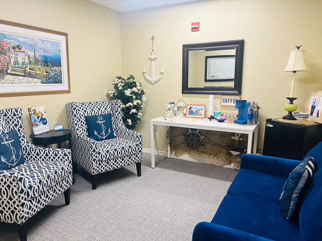 A cozy waiting room with blue and patterned chairs, decorative items, and a mirror on the wall.