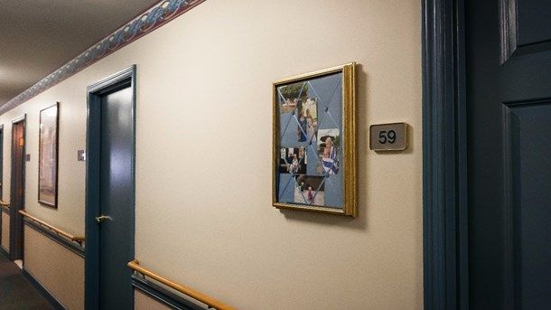 A hallway with framed pictures and a room number sign.