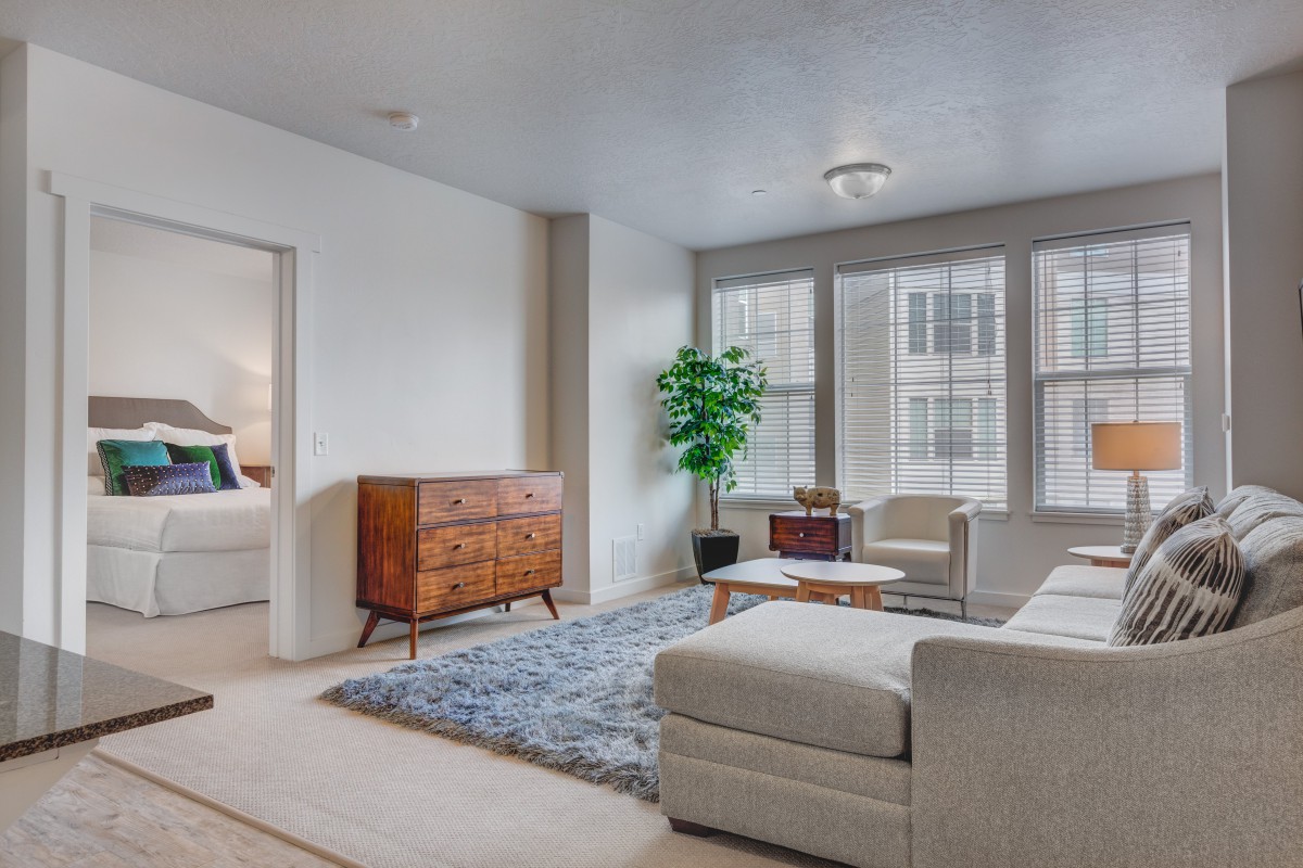 A minimalist living room with a large sofa, wooden furniture, and ample natural light streaming through the windows.