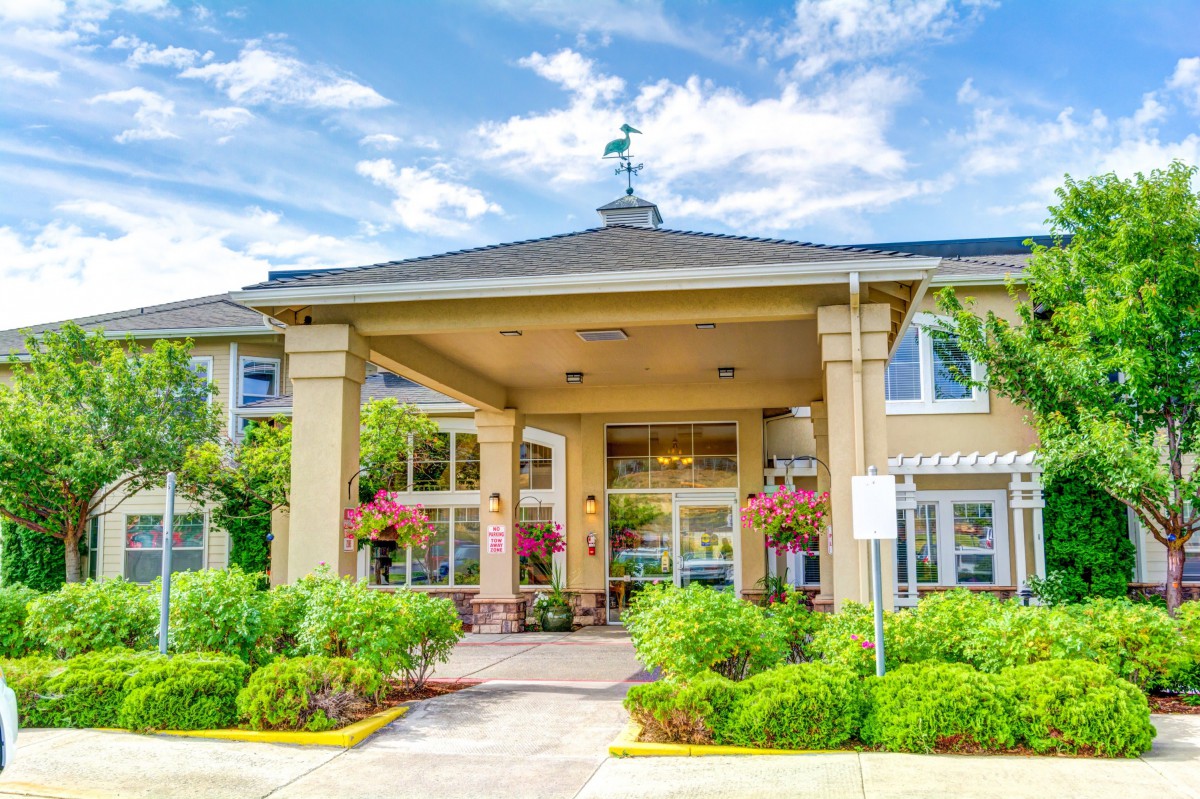 A well-maintained building entrance with lush landscaping under a clear blue sky.