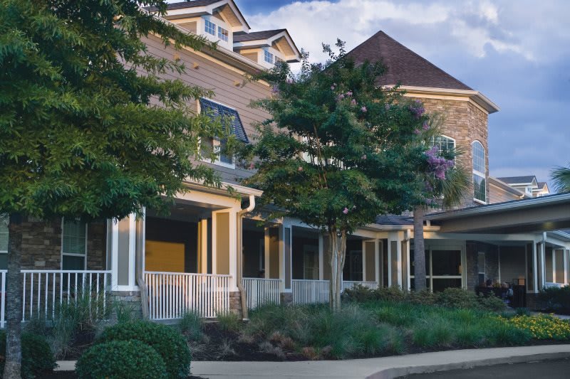 A charming residential house with a welcoming porch and landscaped surroundings.