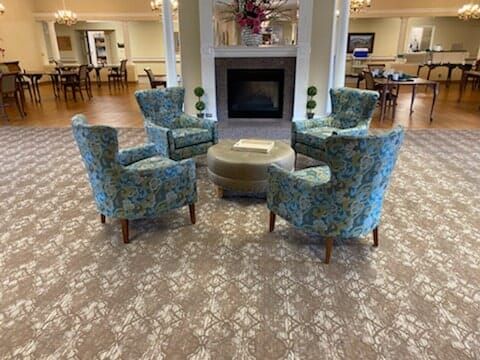 A cozy seating area with patterned chairs arranged around a central ottoman in front of a fireplace.