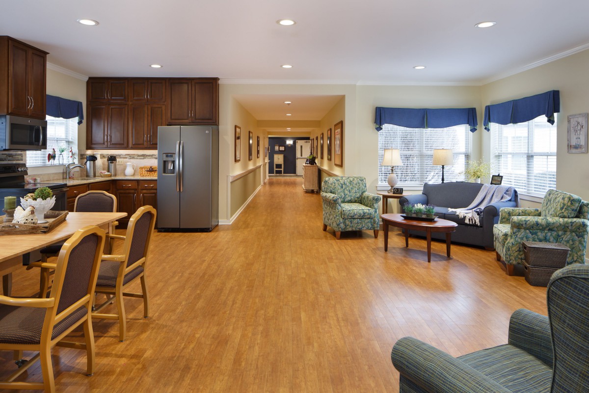 A spacious and well-lit living area with a connected kitchen, featuring cozy seating and wooden flooring.