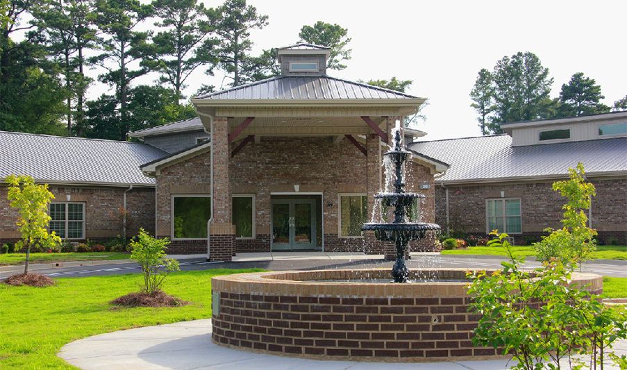 A brick building with a decorative fountain in front and surrounded by greenery.