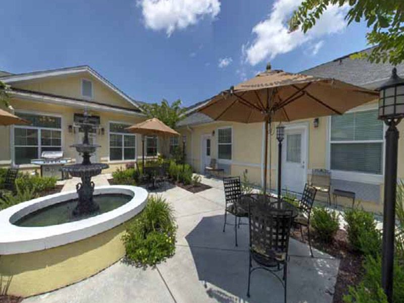 A sunny courtyard featuring outdoor seating, patio umbrellas, and a central fountain.