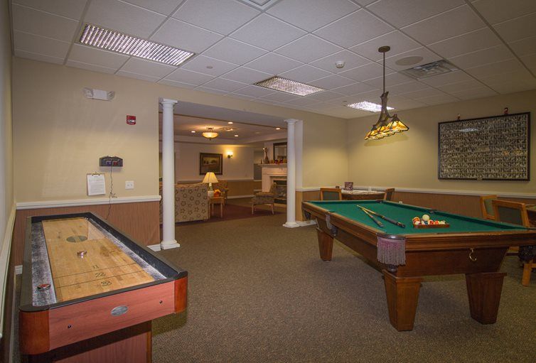 A cozy game room featuring a pool table and shuffleboard under warm indoor lighting.