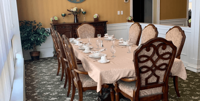 An elegantly set dining table with a beige tablecloth and teacups, surrounded by ornate wooden chairs in a formal dining room.