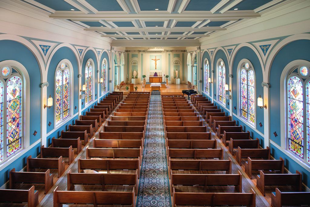 The interior of a church featuring wooden pews, an altar, and colorful stained glass windows.