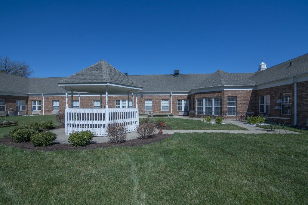 A brick building with a white gazebo in front, surrounded by grass under a clear blue sky.