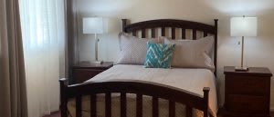 A cozy bedroom with a neatly made bed, featuring neutral bedding and a decorative pillow, accompanied by a bedside lamp.