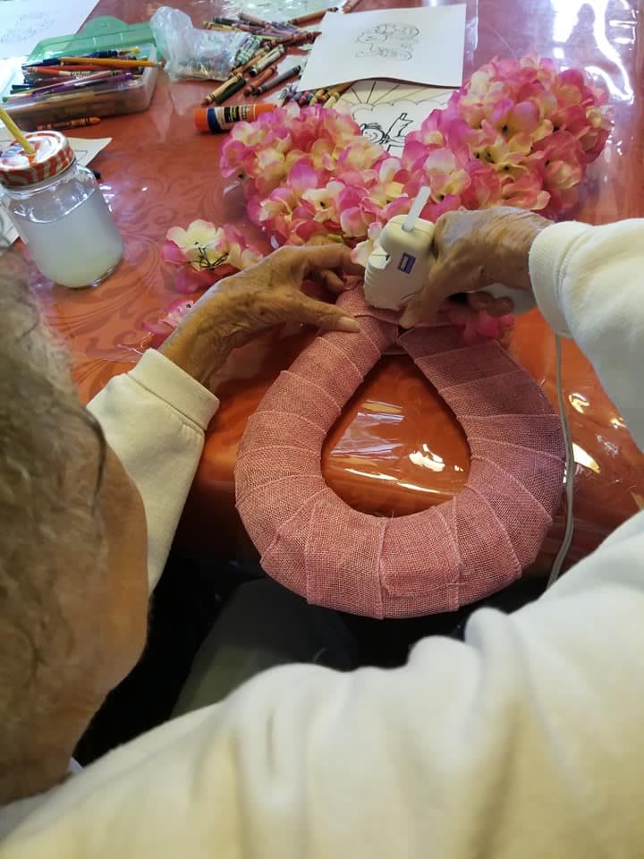 A person crafting a floral lei with pink flowers.