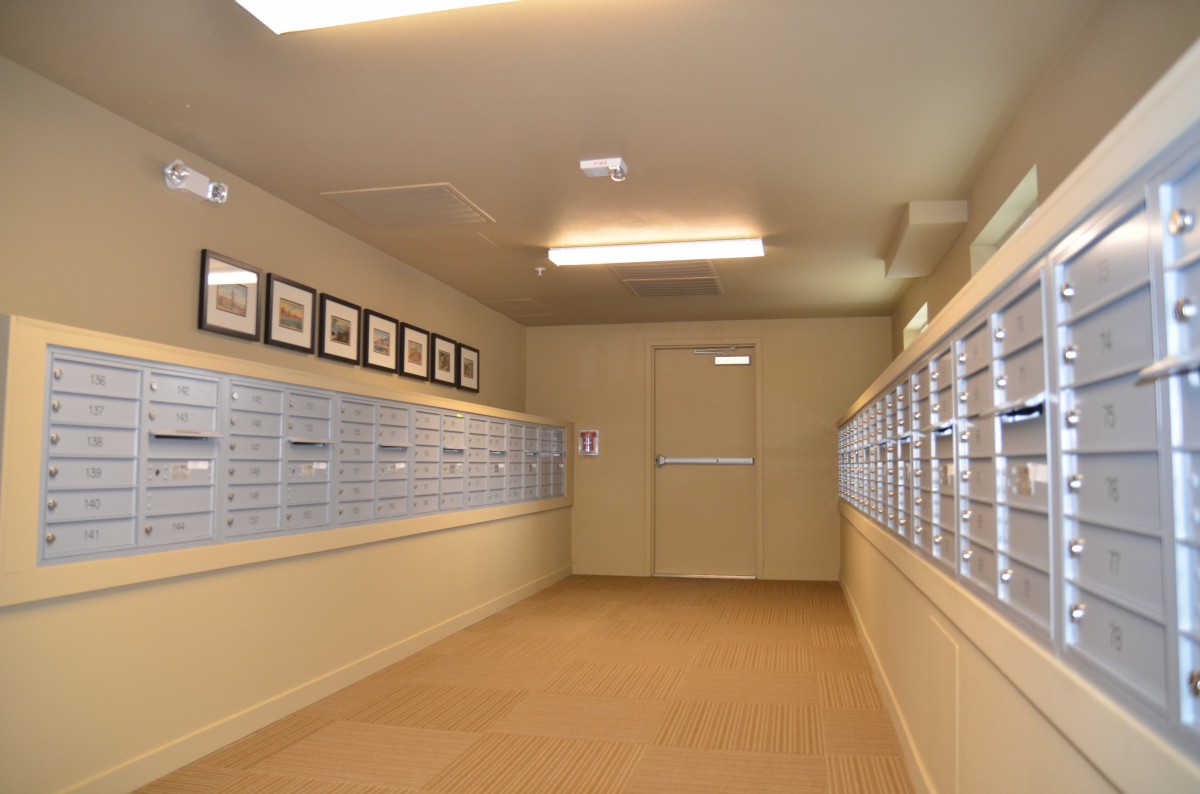 A well-lit corridor featuring rows of postal boxes on each side and framed photographs hanging on the wall.