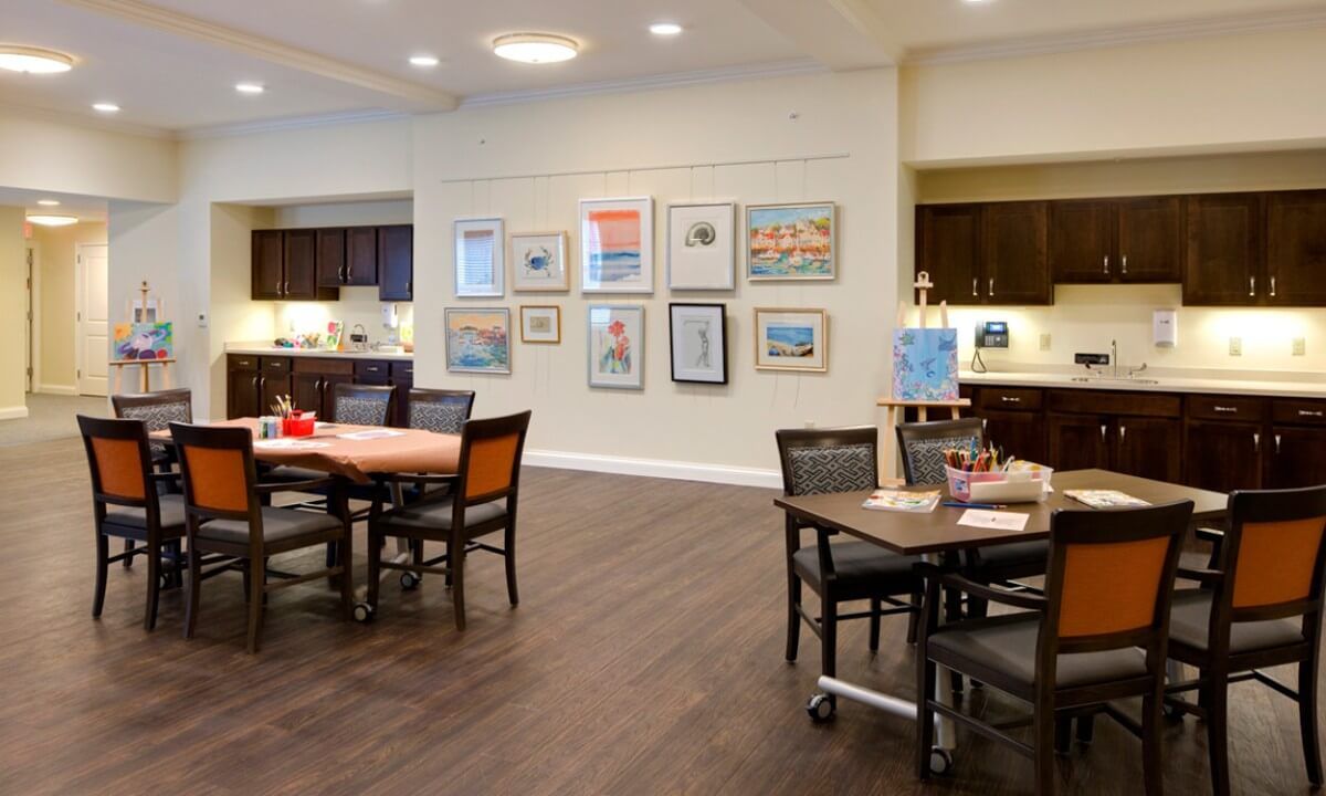 A modern dining area with tables and chairs, featuring wall art and a kitchenette.