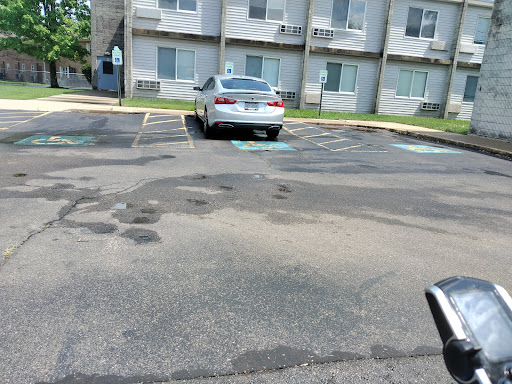 A white car parked in an apartment complex parking lot with visible asphalt patches.