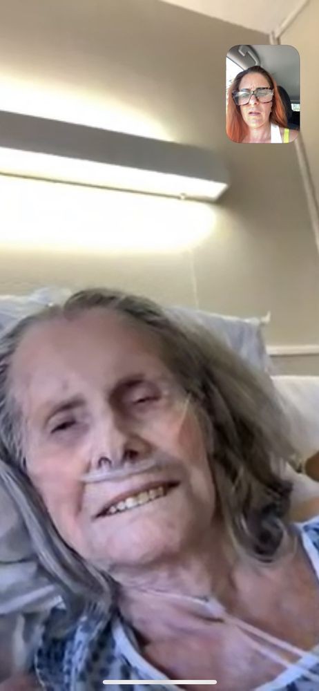 An elderly person smiling while resting in a hospital bed.