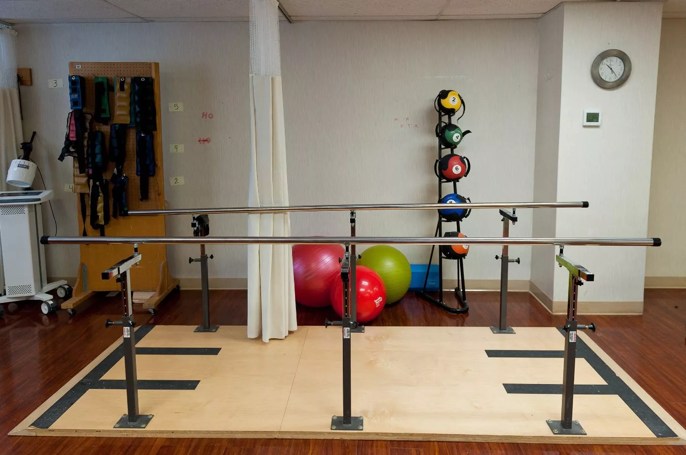 A rehabilitation room equipped with parallel bars and various exercise equipment like medicine balls.