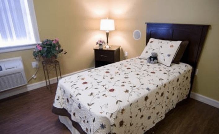 A cozy bedroom featuring a single bed with floral patterned bedding, a bedside lamp, and a nightstand.