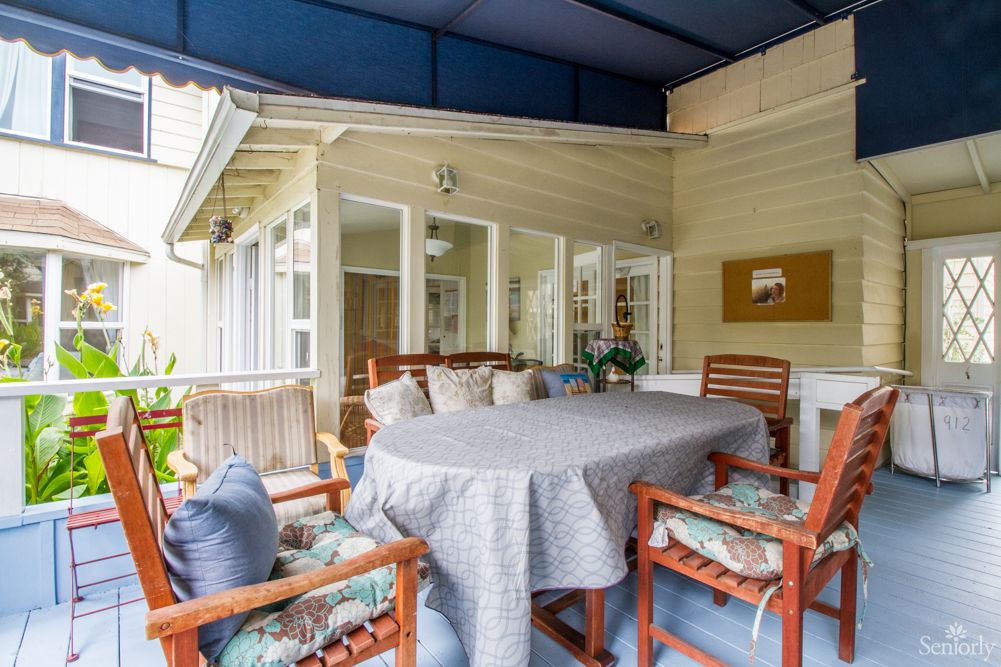 A cozy outdoor patio area with a covered ceiling, featuring a table and cushioned chairs.