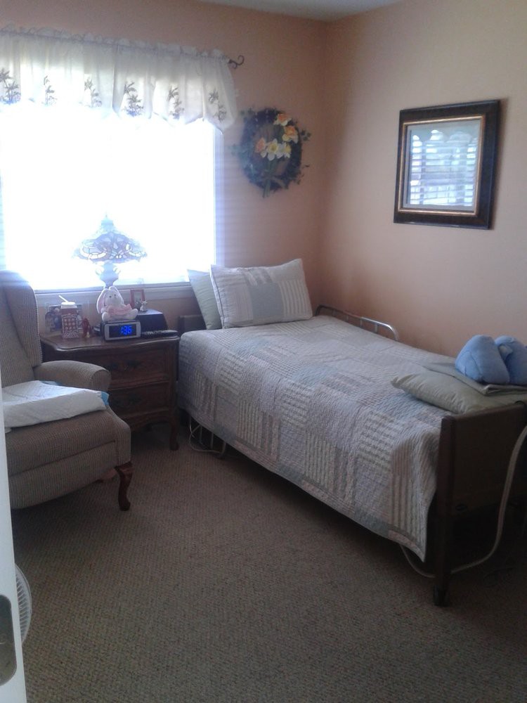 A cozy bedroom with a single bed, armchair, and a side table with a lamp by the window.