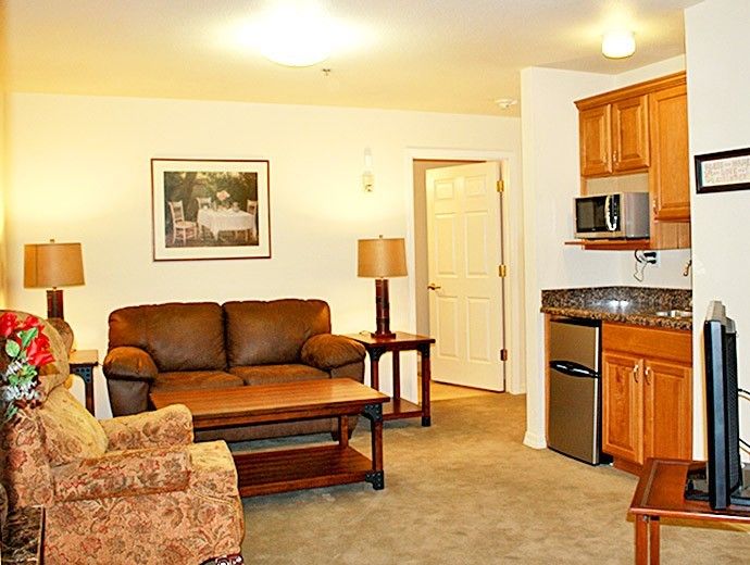A cozy living area with a sofa, armchair, and kitchenette under warm lighting.