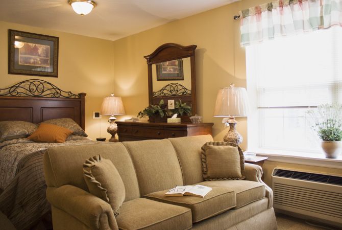 A cozy living room featuring a comfortable sofa, elegant lamps, and classic wooden furniture with a large window allowing natural light.